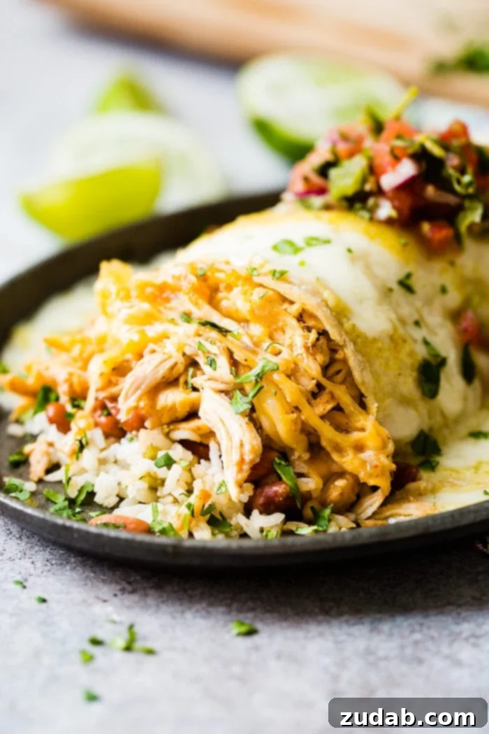 Zesty Honey-Lime Smothered Chicken Burritos 5 A close-up shot of a single, delectable chicken burrito nestled in a cast iron skillet. The burrito is abundantly filled with seasoned rice and beans, and sumptuously topped with melted cheese, fresh salsa, and a scattering of cilantro. Cut limes are artfully placed in the background, adding to the visual appeal.