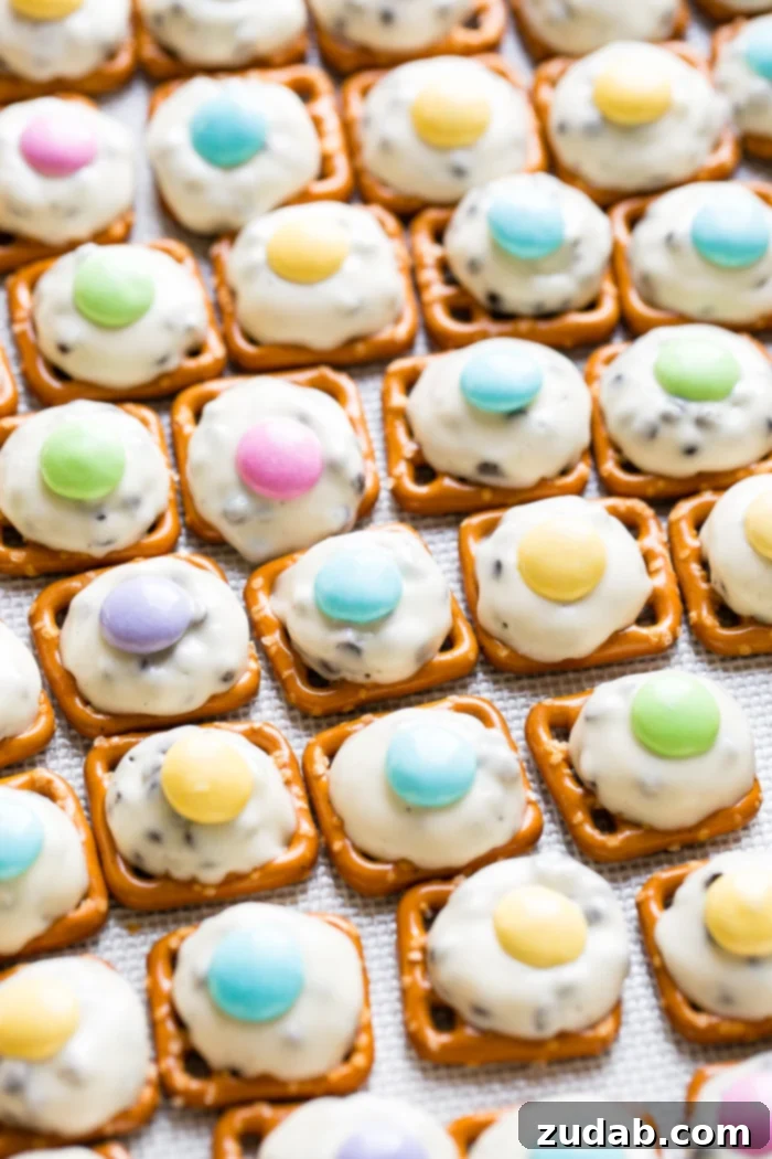 Easter M&M Pretzel Bites 3 Close-up shot of a baking sheet lined with mini pretzels, each adorned with a partially melted Hershey's Hug and a bright Easter-themed M&M, showcasing their simple beauty.