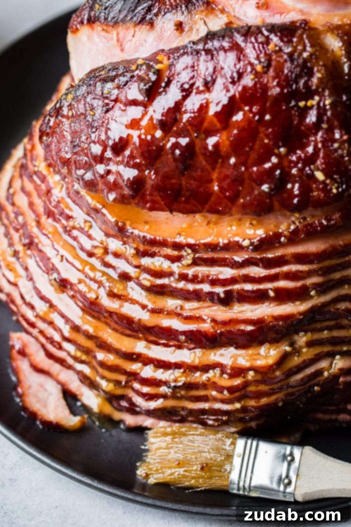 Garlic Honey Mustard Glazed Ham 2 A close up of a spiral glazed honey mustard ham on a black platter with a basting brush, showcasing its beautiful, golden-brown glaze.