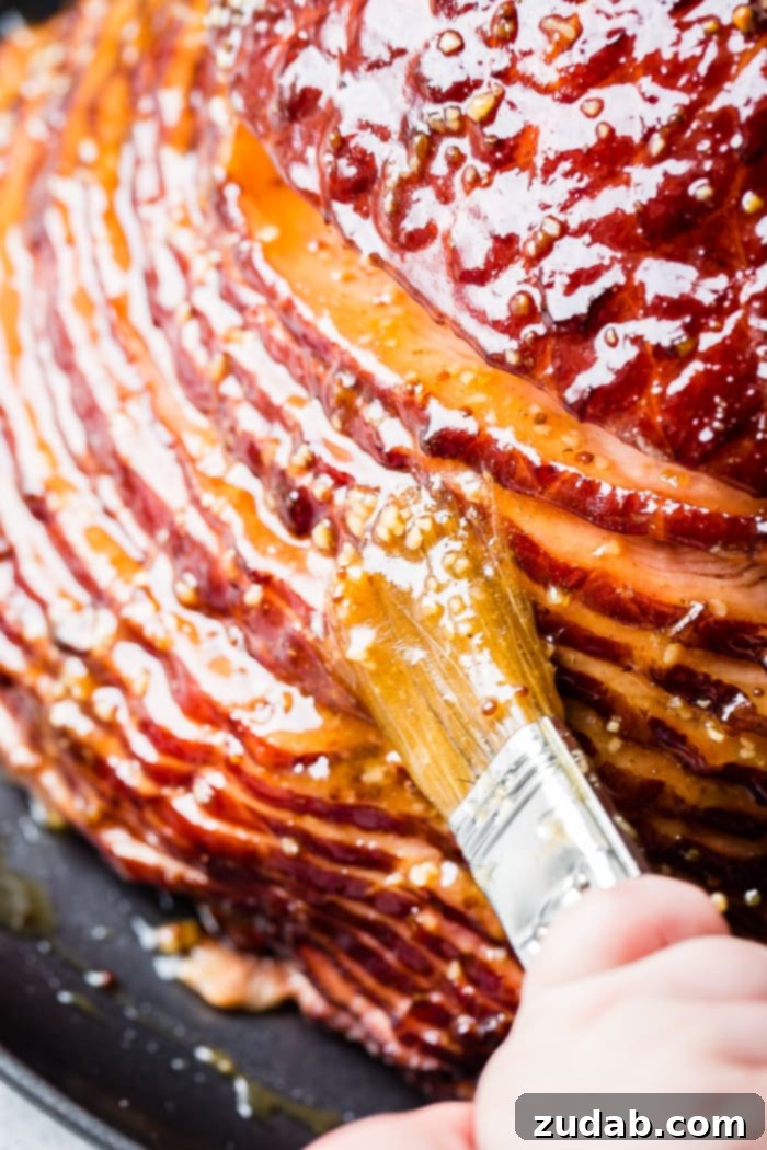 Garlic Honey Mustard Glazed Ham 4 A close-up shot of the beautifully glazed garlic honey mustard spiral ham on a black platter, glistening with its rich, aromatic glaze, alongside a basting brush.