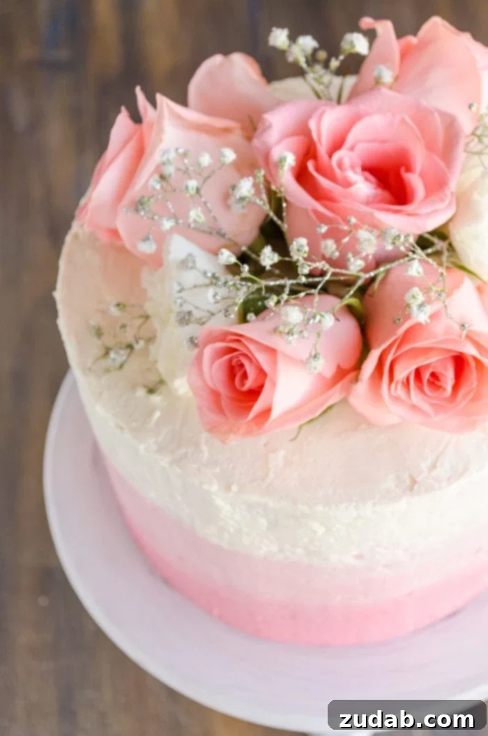 Blushing Strawberry Ombre Cake 13 An overhead shot captures a stunning three-layer ombre Mothers Day strawberry cake, adorned with fresh pink roses and sparkling sprigs of baby's breath, ready for celebration.