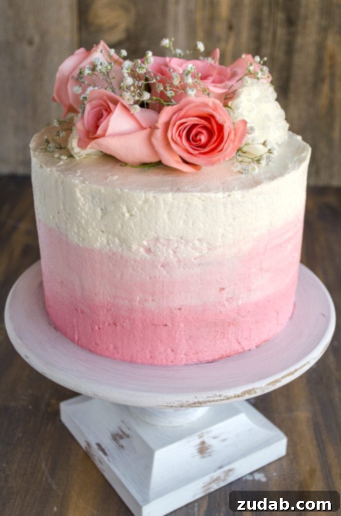 Blushing Strawberry Ombre Cake 14 A stunning three-layer ombre Mothers Day strawberry cake, adorned with fresh pink roses and sparkling sprigs of baby's breath, sitting atop a rustic white raised cake dish.