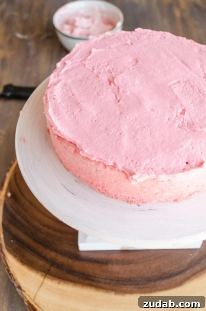 Blushing Strawberry Ombre Cake 8 The darkest pink layer of this cake is placed on a raised cake stand and topped with a matching dark pink frosting, awaiting the next layer.