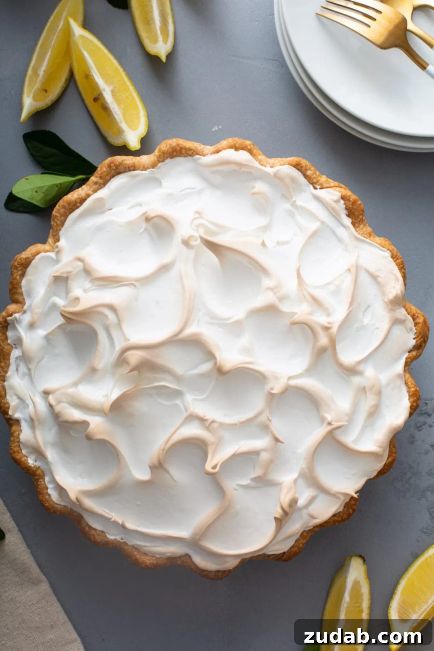 Delicious Homemade Lemon Meringue Pie A top-down view of a completed lemon meringue pie, with its beautifully toasted, fluffy meringue topping. A few fresh lemon wedges are placed invitingly next to the pie.