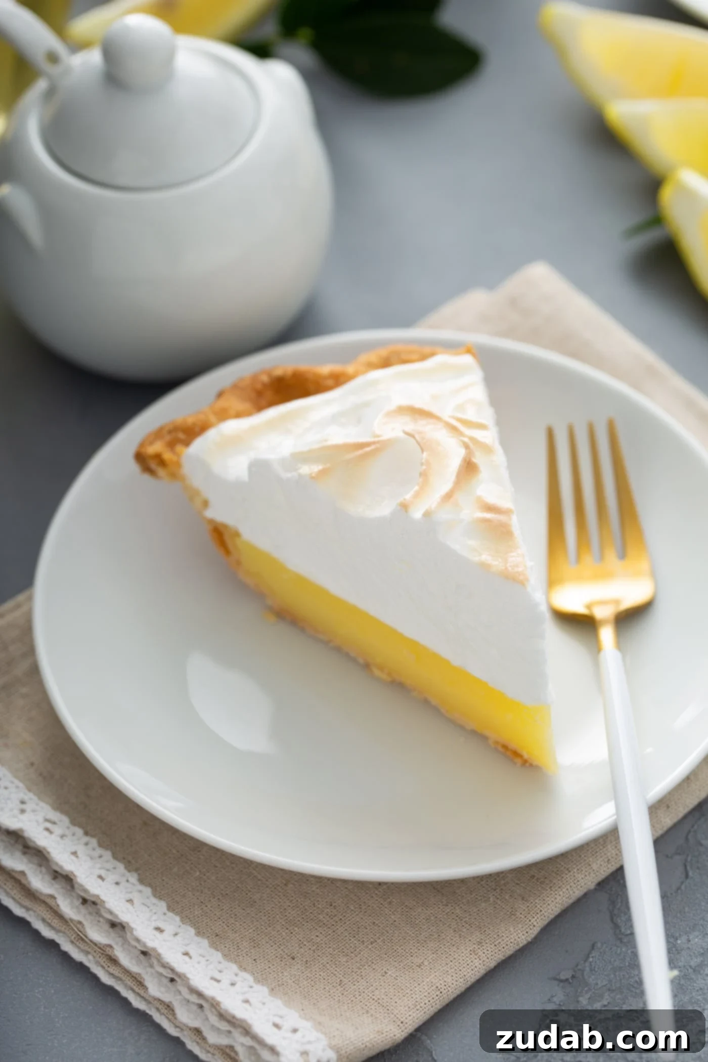 A Mouthwatering Lemon Meringue Pie Slice A perfect slice of lemon meringue pie on a white dessert plate, with a fork ready for a bite. A classic sugar bowl is subtly visible in the background.