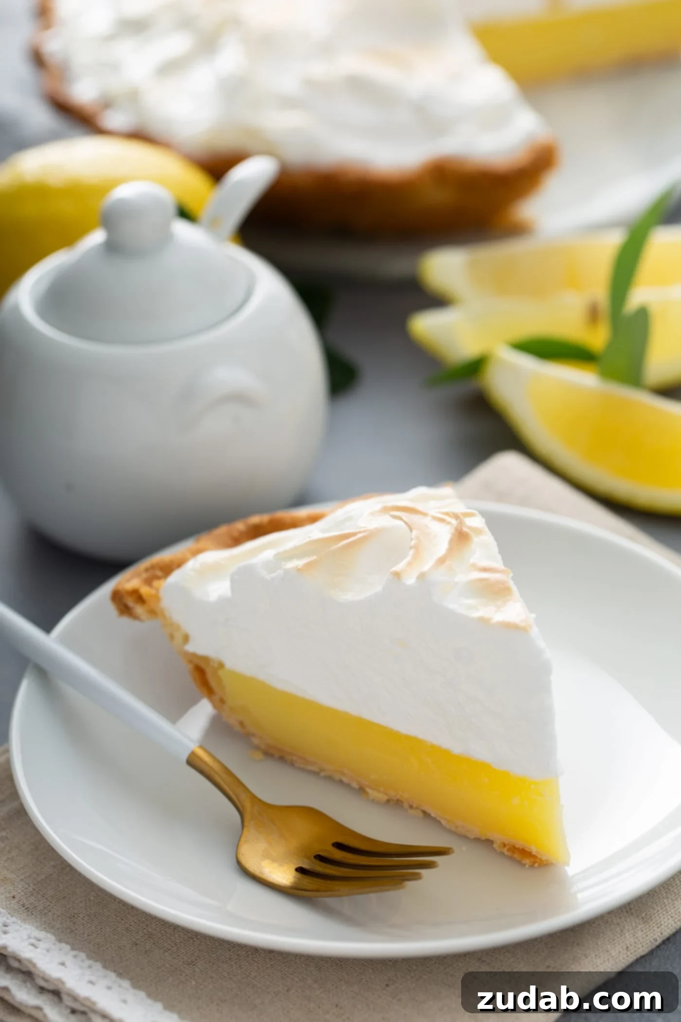 Mom's Irresistible Lemon Meringue Pie A close-up shot of a perfect slice of lemon meringue pie on a white plate. The bright yellow filling contrasts beautifully with the lightly toasted, billowy meringue. Lemon wedges and a sugar bowl are visible in the soft-focus background, with a fork poised for a delicious bite.
