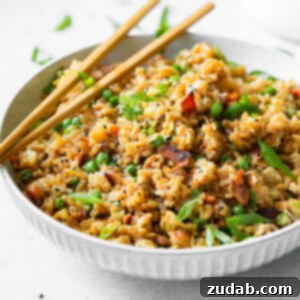 A close-up of a bowl of Bacon Fried Rice, showcasing crispy bacon bits, peas, carrots, and egg.