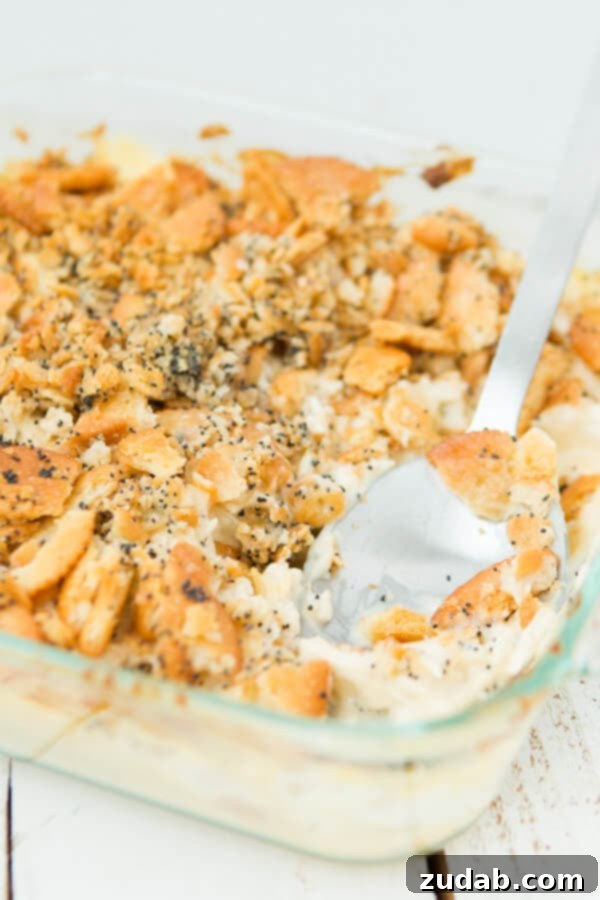 Everyone's favorite Poppy Seed Chicken Casserole with ritz crackers ohsweetbasil.com scooping poppy seed chicken casserole out of a glass baking dish