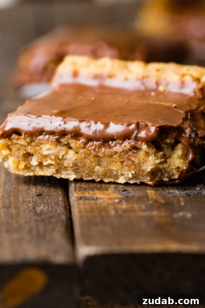 Irresistible Peanut Butter Bars 4 A single, perfectly cut Peanut Butter Bar topped with luscious chocolate frosting, resting on a wooden surface, ready to be enjoyed.