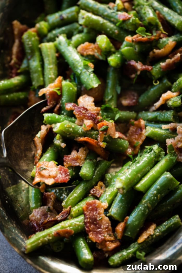 Quick Bacon Green Beans 3 A silver serving platter and matching serving spoon delving into a bowl of perfectly cooked green beans with crumbled bacon.
