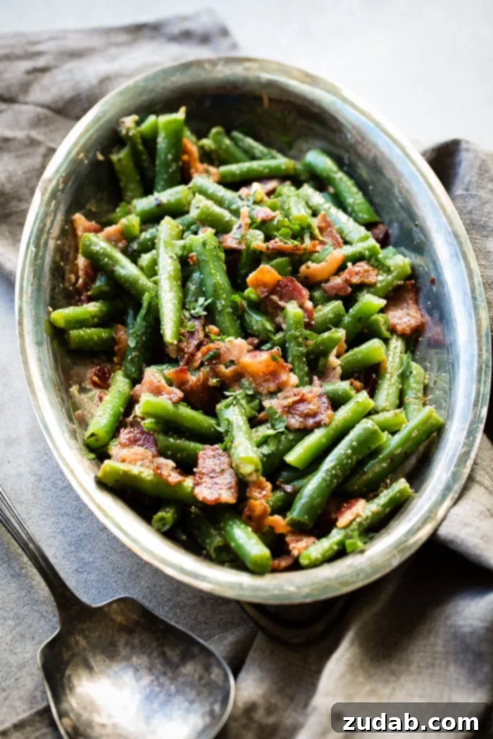 Quick Bacon Green Beans 4 Chopped green beans with crumbled, crispy bacon pieces, elegantly presented in a silver serving platter alongside a grey napkin and a vintage silver serving spoon.