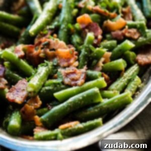 A silver serving dish with bright green beans that have been chopped and served with crumbled bacon.