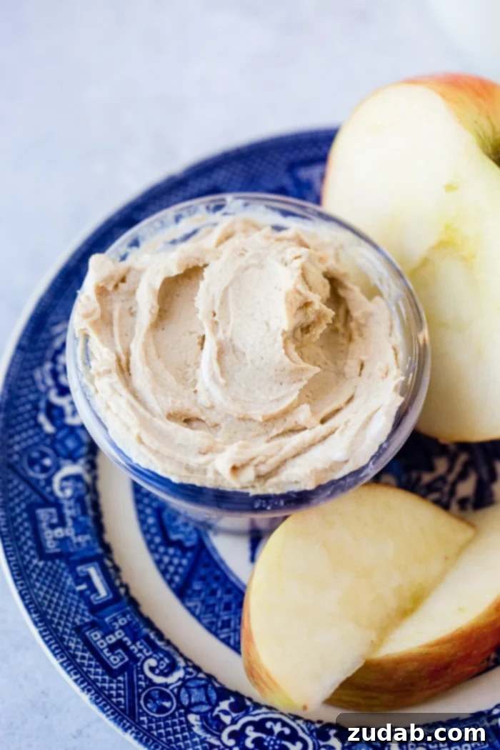 Creamy Peanut Butter Greek Yogurt Dip 3 A close-up shot of a blue dish displaying perfectly sliced apple pieces and a half apple, with a small ceramic bowl brimming with creamy, healthy peanut butter Greek yogurt dip.