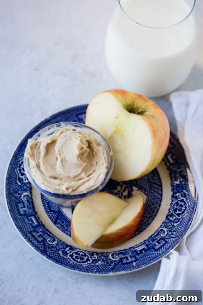 Creamy Peanut Butter Greek Yogurt Dip 4 A blue ceramic dish beautifully arranged with thinly sliced apple wedges and a half apple, accompanied by a small, inviting bowl of creamy peanut butter Greek yogurt dip, ready for a healthy snack.
