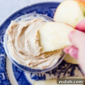 A blue dish holding a sliced apple and half of an apple with a small dish of healthy peanut butter greek yogurt dip