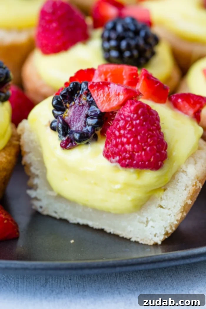Zesty Lemon Fruit Cookie Cups 3 A dark pan with sugar cookie cups filled with lemon filling and topped with blackberries, raspberries and chopped strawberries
