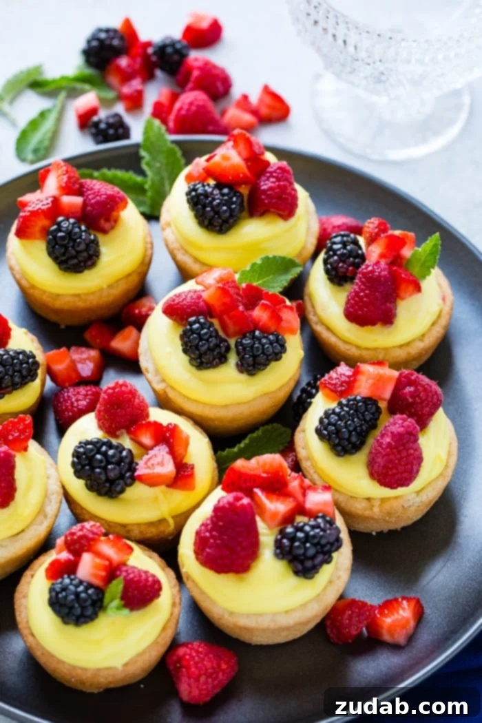 Zesty Lemon Fruit Cookie Cups 4 A dark pan with sugar cookie cups filled with lemon filling and topped with blackberries, raspberries and chopped strawberries