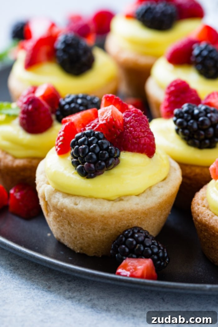 Zesty Lemon Fruit Cookie Cups 5 A dark pan with a close up of a sugar cookie cups filled with lemon filling and topped with blackberries, raspberries and chopped strawberries