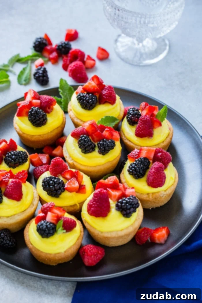 Zesty Lemon Fruit Cookie Cups 7 A dark pan with sugar cookie cups filled with lemon filling and topped with blackberries, raspberries and chopped strawberries