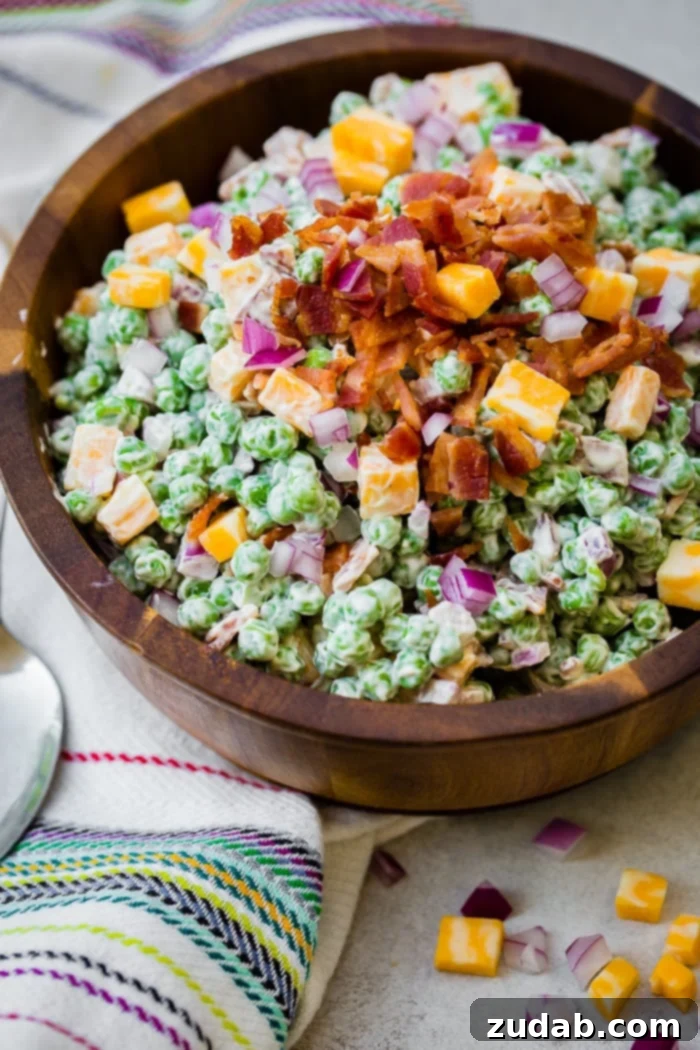 Creamy Southern Pea Salad 4 a wooden bowl full of creamy southern english pea salad with bacon, chunks of colby jack cheese and a metal spoon sitting on the side
