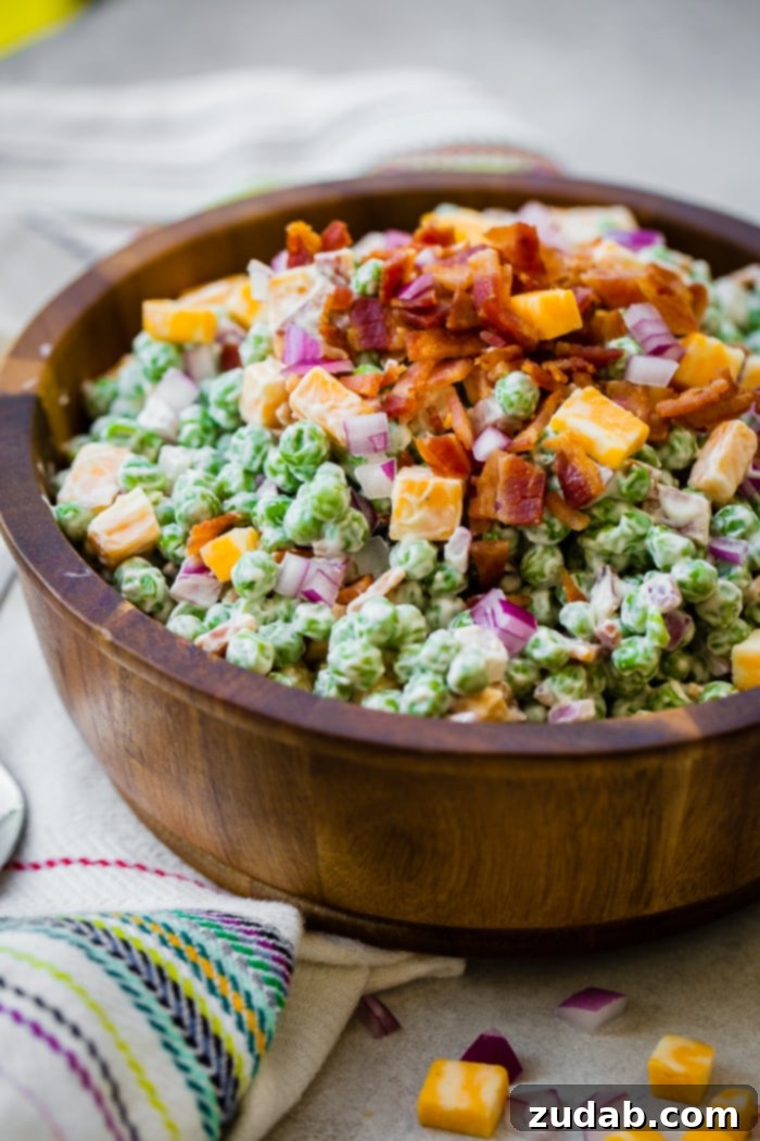 Creamy Southern Pea Salad 5 a wooden bowl full of creamy southern english pea salad with bacon, chunks of colby jack cheese