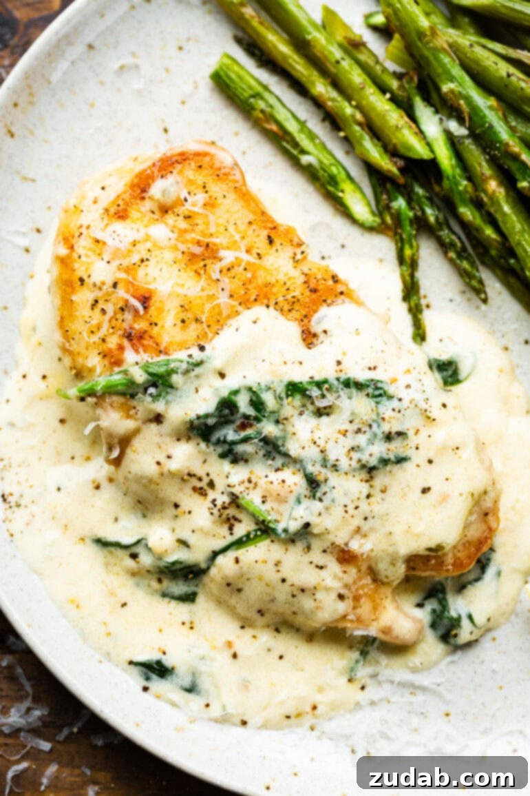 Chicken Florentine 8 A serving of golden pan-seared chicken breast covered in a creamy sauce and spinach, next to a serving of asparagus