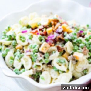 A white bowl with orchiette pasta, peas, cubed colby jack cheese, red onion and a simple dressing for the recipe southern pea pasta salad