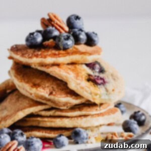 A stack of blueberry pecan pancakes with a drizzle of maple syrup