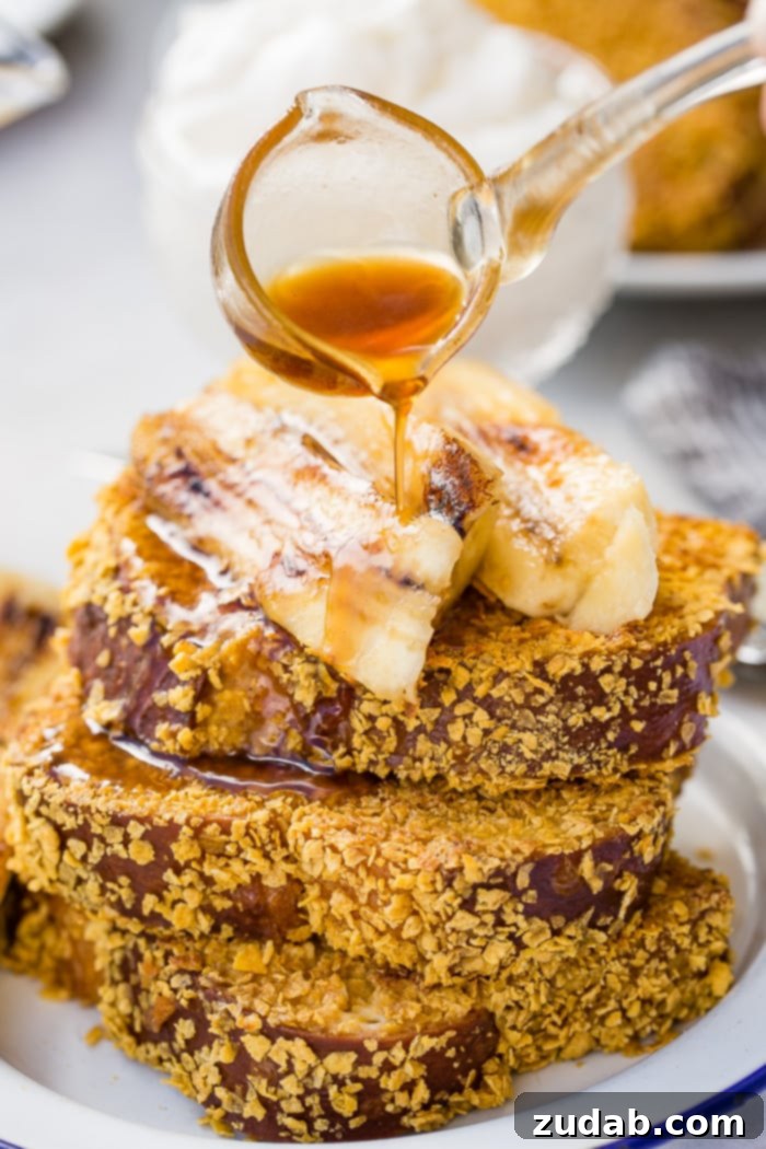 Cade's Signature Bananas Foster French Toast 8 Golden brown cornflake-crusted French toast on a plate, with rich bananas foster syrup being drizzled over the top.