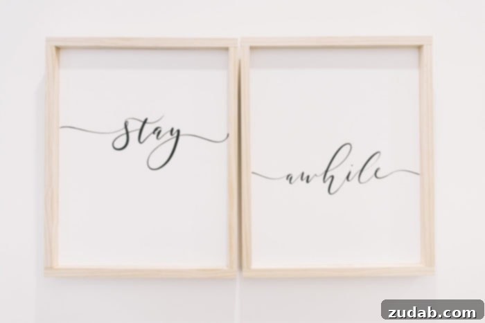 Stunning Basement Bedroom Makeovers 7 Two framed wooden signs on a crisp white wall, one above the other, with the words 'stay awhile' in elegant script. The natural wood frames add warmth and a welcoming touch to the guest bedroom decor.