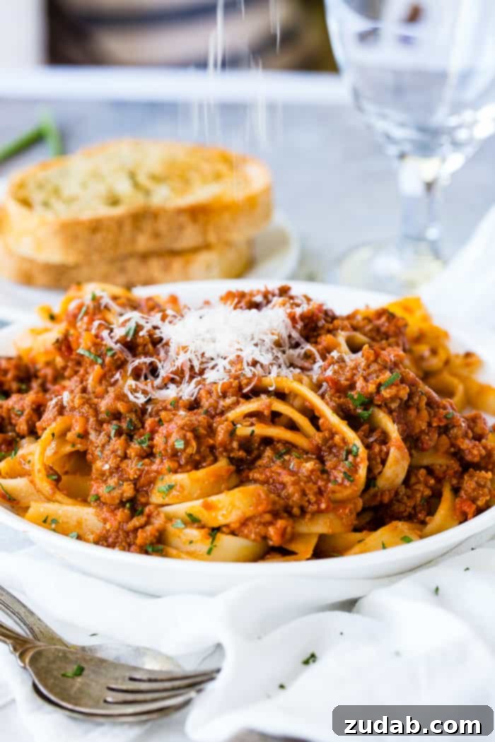 Mastering Authentic Italian Bolognese 2 A beautifully plated dish of fettuccine pasta generously coated with rich, authentic Italian Bolognese sauce, topped with grated Parmesan cheese, with a side of golden garlic bread in the background.