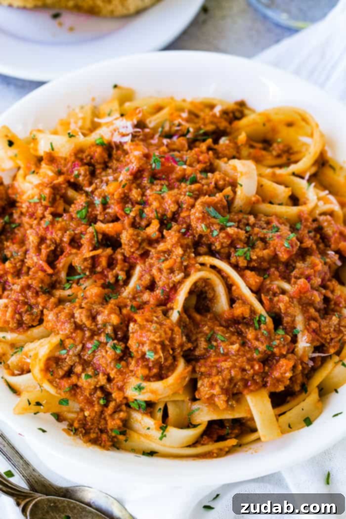 Mastering Authentic Italian Bolognese 3 A close-up shot of fettuccine pasta generously topped with rich, authentic Italian Bolognese sauce, highlighting the hearty texture of the meat sauce.