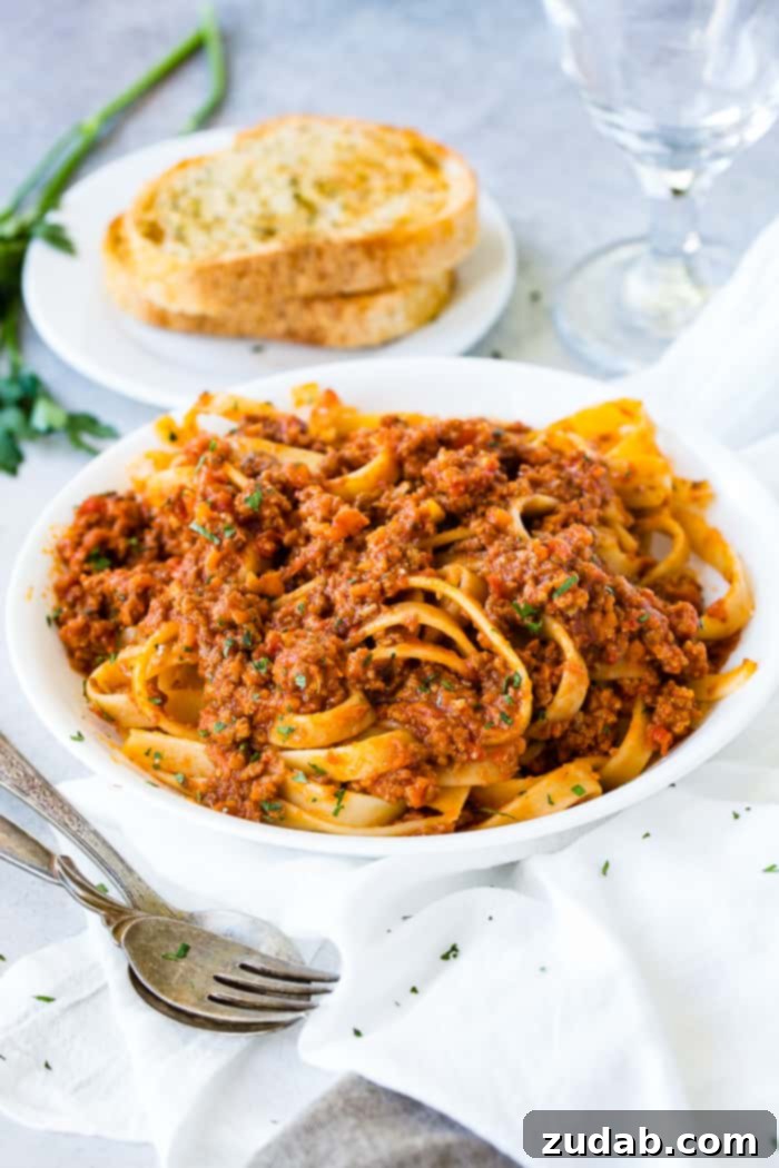 Mastering Authentic Italian Bolognese 4 A serving of broad fettuccine pasta coated with rich Bolognese sauce, showing the sauce clinging perfectly to the noodles.