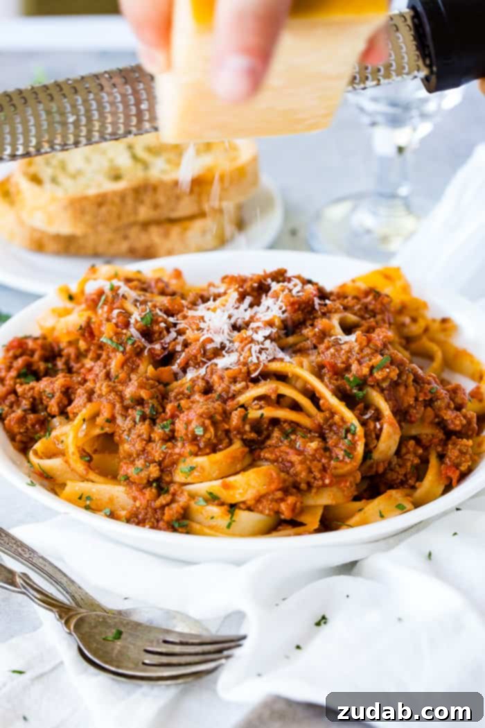 Mastering Authentic Italian Bolognese 5 A delectable bowl of fettuccine pasta generously covered in authentic Italian Bolognese sauce, topped with grated Parmesan cheese, with a side of crispy garlic bread.