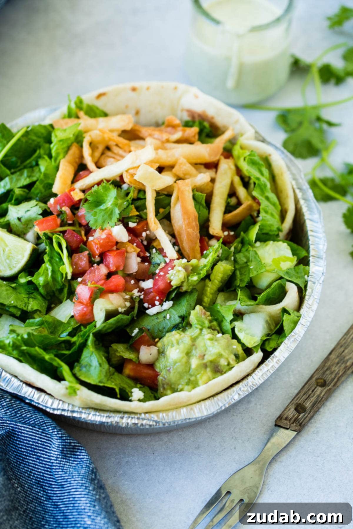 An overhead view of a vibrant copycat Cafe Rio chicken salad, generously topped with pico de gallo, crispy tortilla strips, homemade guacamole, and a fresh lime wedge.