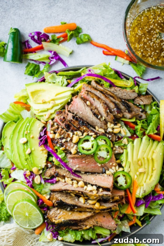Grilled Flank Steak with Zesty Thai Peanut Salad 5 A colorful bowl of mixed greens, freshly chopped veggies, and tender flank steak marinated in peanut sauce. A vibrant ginger dressing with sesame seeds is drizzled over the salad.