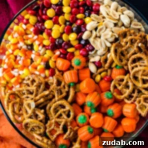 A delicious 5 Minute Halloween Snack Mix in a white bowl, ready to be served. Features candy corn, pretzels, M&M's, peanuts, and candy pumpkins.