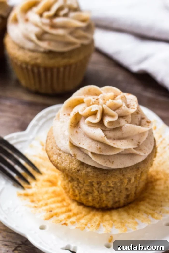 Fragrant Spice Cupcakes with Zesty Cinnamon Cream Cheese Frosting 2 A moist spice cake cupcake topped with cream cheese frosting on a white plate, invitingly ready to be enjoyed.