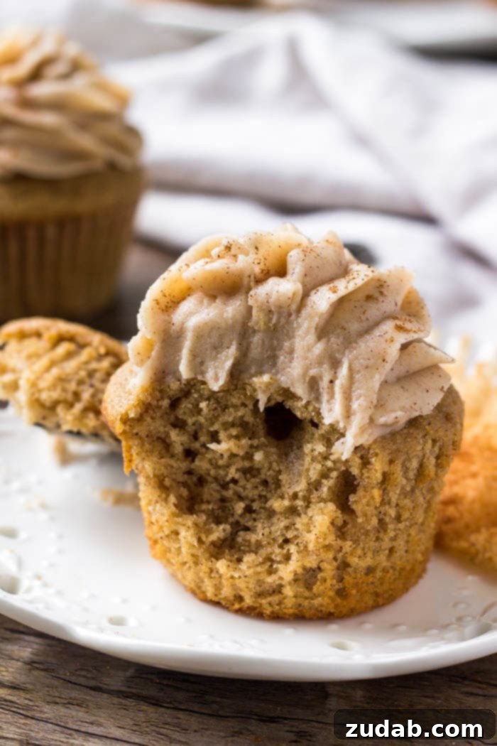 Fragrant Spice Cupcakes with Zesty Cinnamon Cream Cheese Frosting 6 A delectable spice cake cupcake, generously topped with cinnamon cream cheese frosting, with a tempting bite taken out to reveal its moist interior.