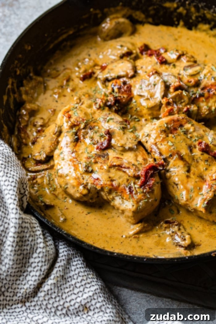 Effortless Creamy Herb Chicken with Sun-Dried Tomatoes 4 A black cast iron skillet with a creamy sauce full of sun dried tomatoes, mushrooms and seasoning over perfectly cooked chicken, ready to be served.