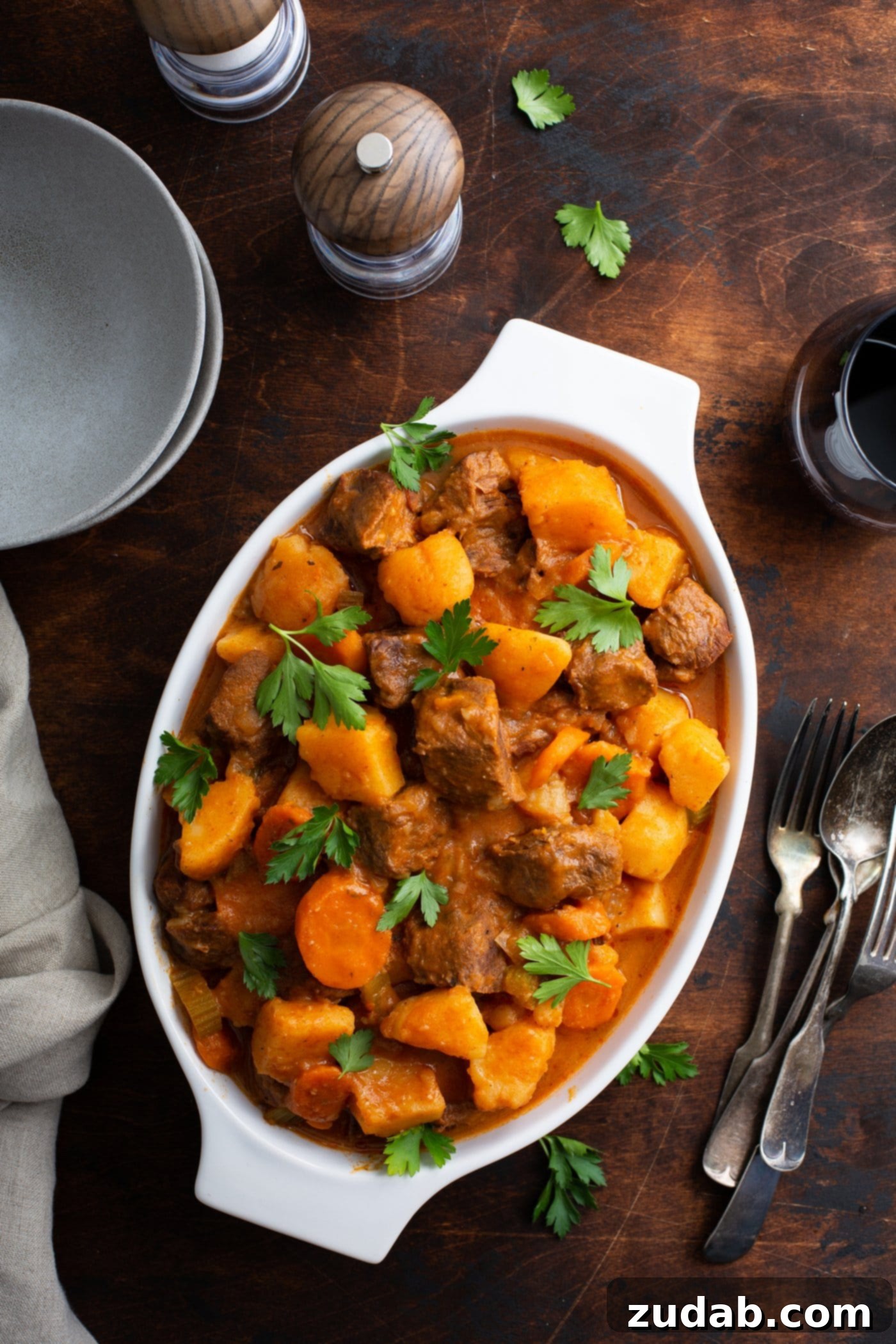 Instant Pot Beef Stew A serving bowl of instant pot beef stew. There are chunks of beef, carrots, and potatoes with fresh parsley sprinkled on top. Bowls and spoons are in the background.