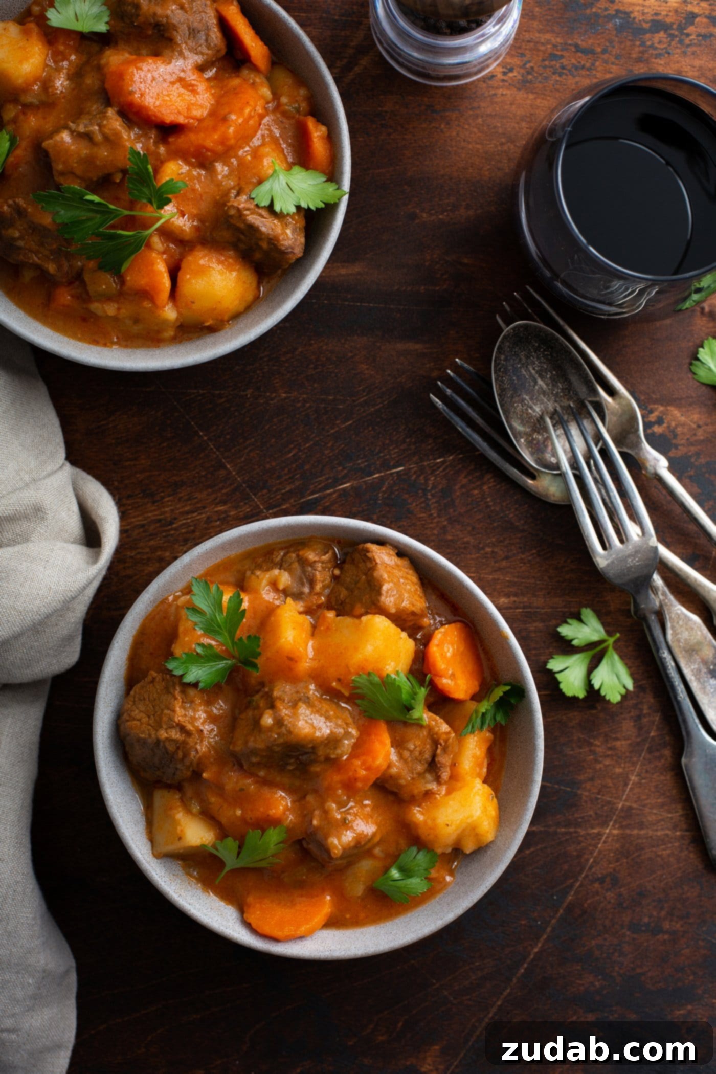 Instant Pot Beef Stew Two bowl of instant pot beef stew. there are chunks of beef, carrots, and potatoes in a rich brown gravy. The stew is sprinkled with fresh parsley leaves, and there are forks and spoons next to the bowls.