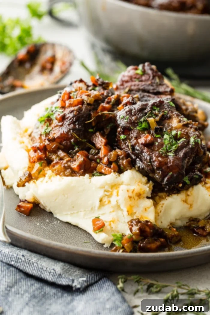Melt-in-Your-Mouth Oven Braised Short Ribs 4 A dark grey plate with a pile of creamy mashed potatoes with fall apart braised beef short ribs and fresh parsley