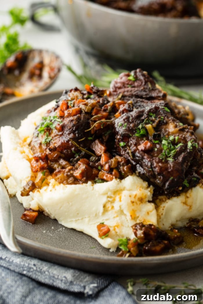 Melt-in-Your-Mouth Oven Braised Short Ribs 5 A dark grey plate with a pile of creamy mashed potatoes with fall apart braised beef short ribs and fresh parsley