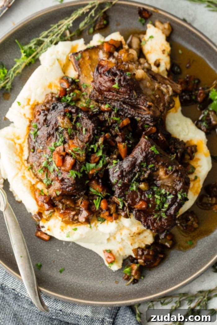 Melt-in-Your-Mouth Oven Braised Short Ribs 6 A dark grey plate with a pile of creamy mashed potatoes with fall apart braised beef short ribs and fresh parsley