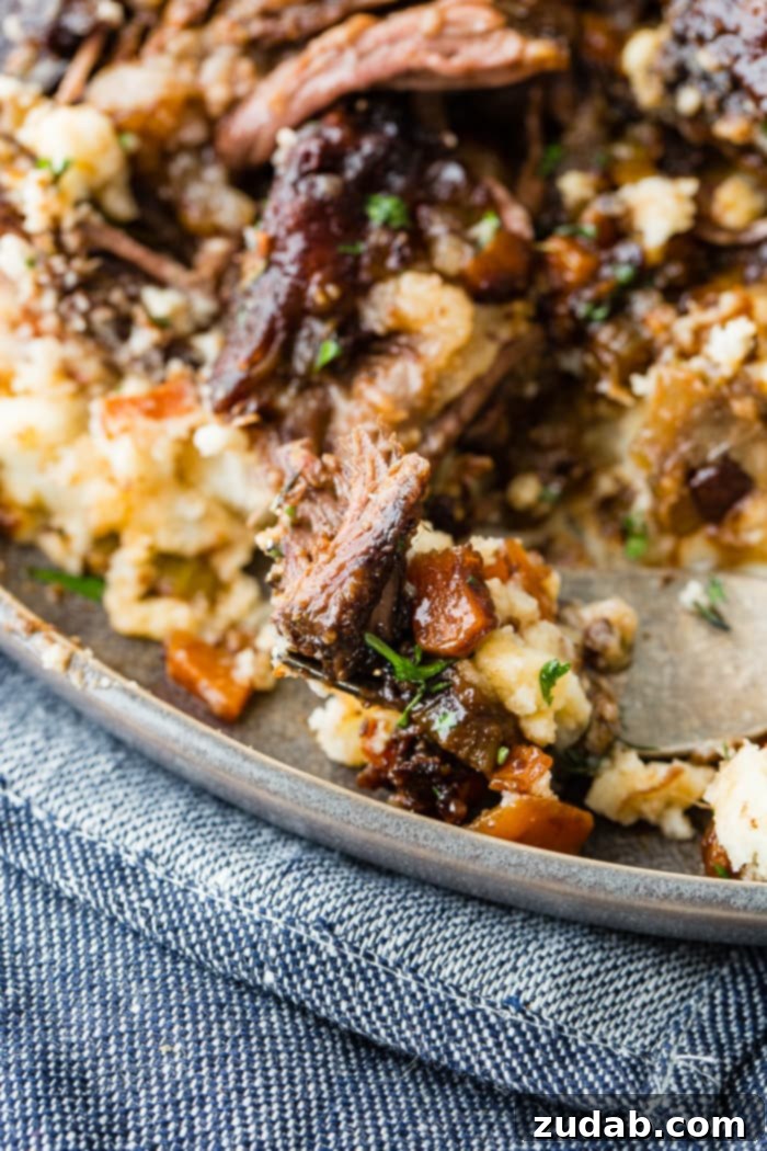 Melt-in-Your-Mouth Oven Braised Short Ribs 7 A dark grey plate with a pile of creamy mashed potatoes with fall apart braised beef short ribs and fresh parsley