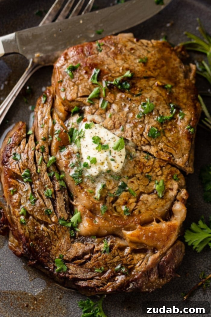 Savor Delicious Garlic Butter Steak, Effortlessly at Home 3 a grey plate with a medium rare ribeye steak being cut into and a fork taking a piece with garlic butter melting on top with parsley