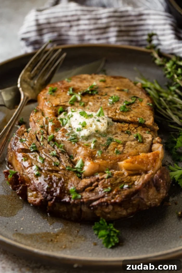 Savor Delicious Garlic Butter Steak, Effortlessly at Home 4 a grey plate with a medium rare ribeye steak being cut into and a fork taking a piece with garlic butter melting on top with parsley