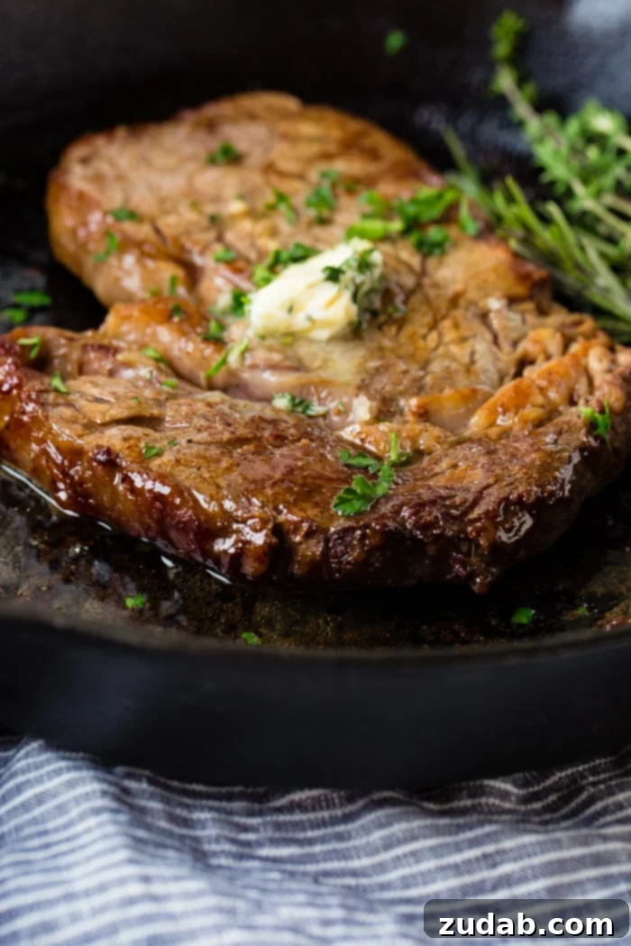 Savor Delicious Garlic Butter Steak, Effortlessly at Home 5 a grey plate with a medium rare ribeye steak being cut into and a fork taking a piece with garlic butter melting on top with parsley