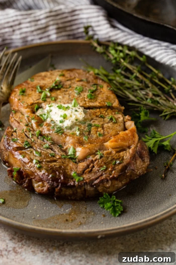 Savor Delicious Garlic Butter Steak, Effortlessly at Home 6 a grey plate with a medium rare ribeye steak being cut into and a fork taking a piece with garlic butter melting on top with parsley